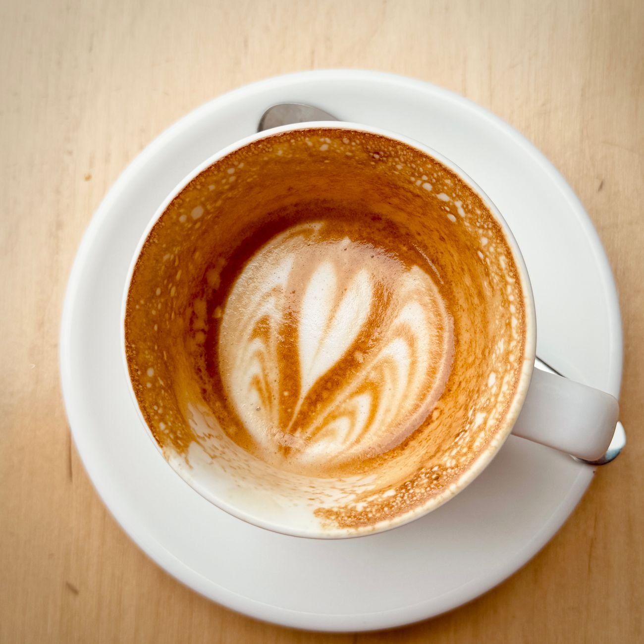 Empty coffee cup displaying intricate latte art on a wooden table.