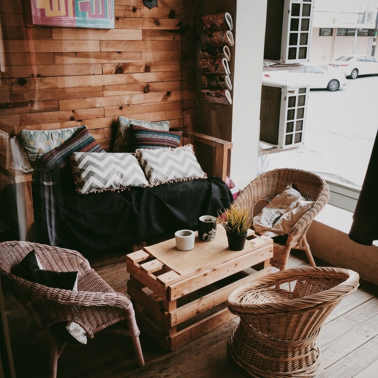 Warm and inviting café corner featuring wooden and woven furniture with pillows. Ideal for cozy retreats.